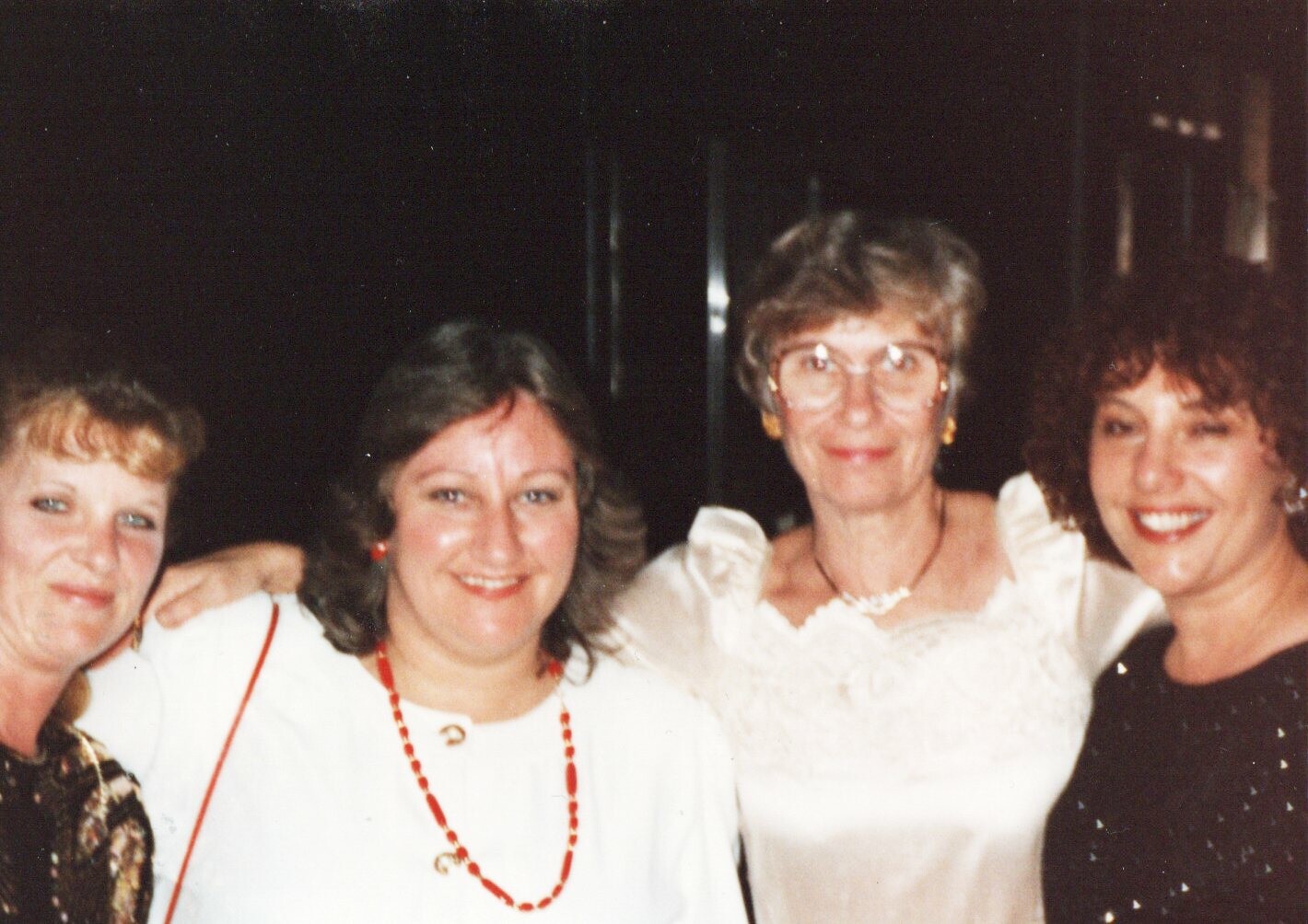 Four women posing together at a social event, smiling at the camera.