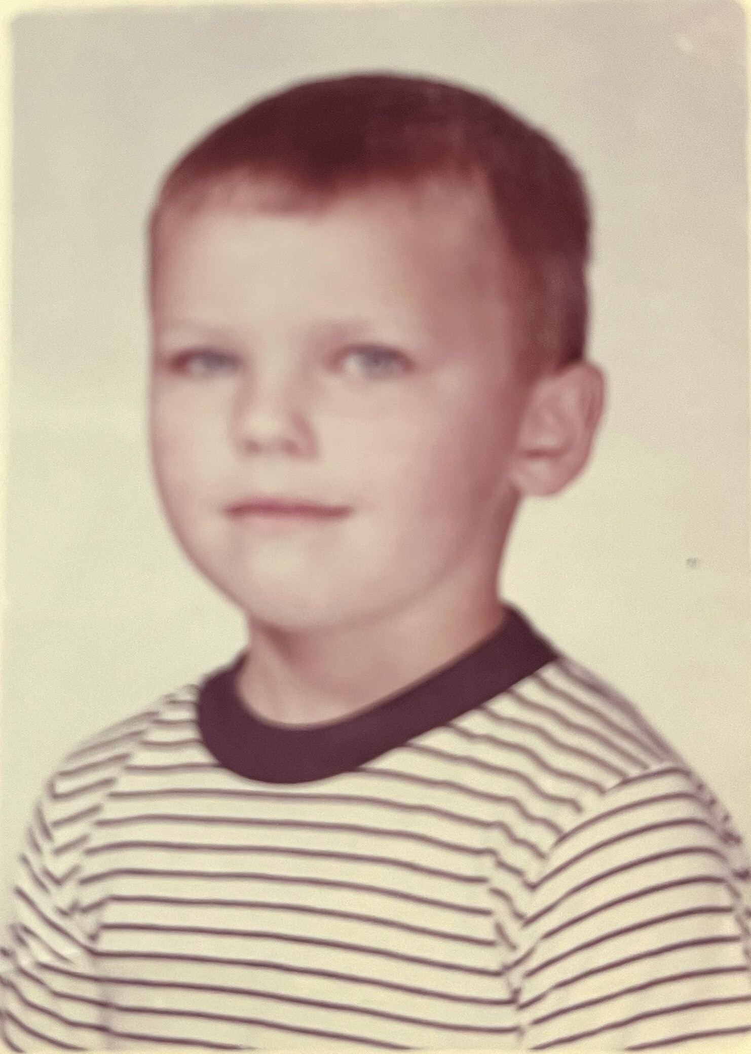 Portrait of a young boy with short brown hair wearing a striped shirt, looking toward the camera.