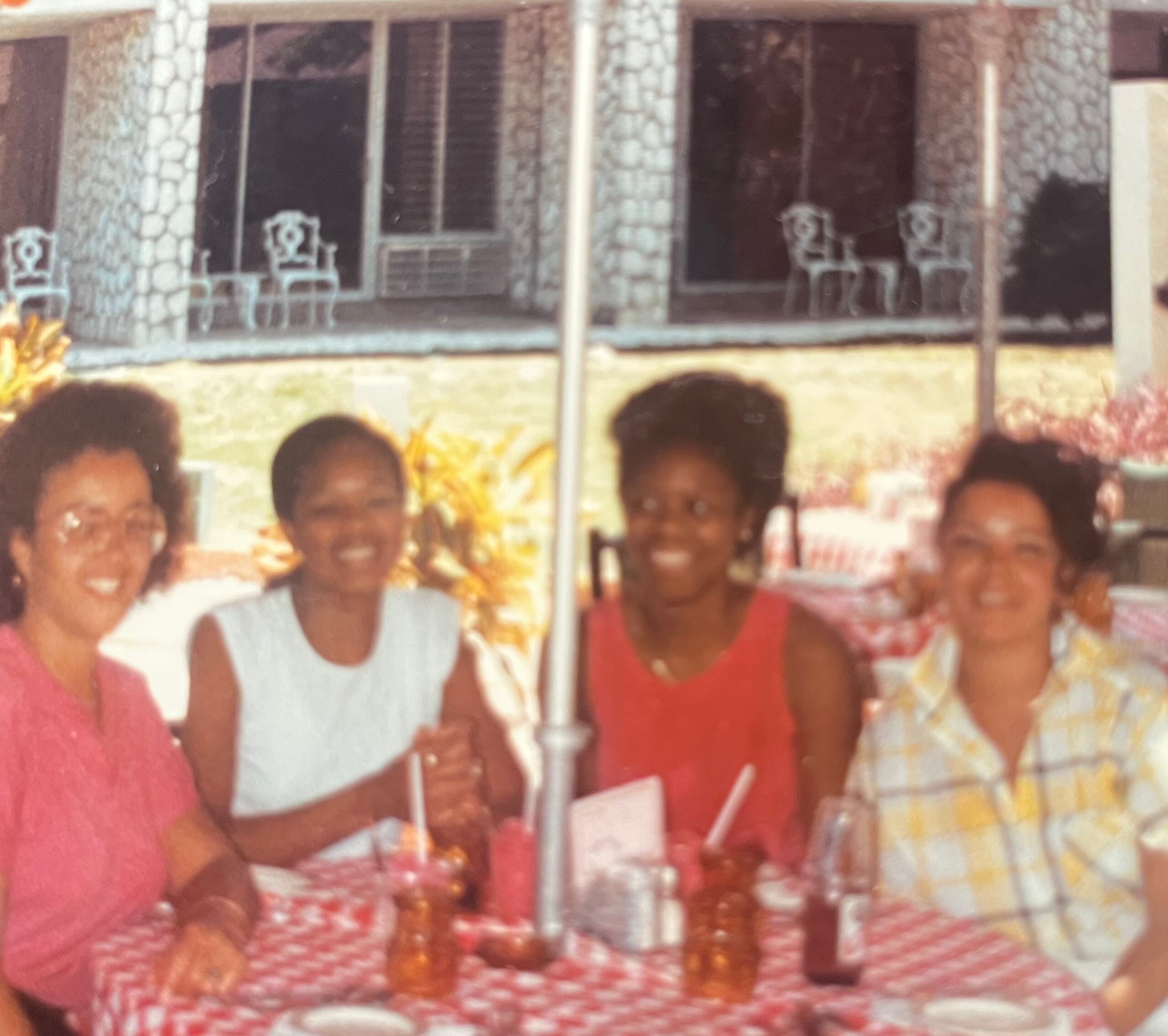 Group of people smiling and posing for a photo on a covered patio with stone pillars and chairs in the background.