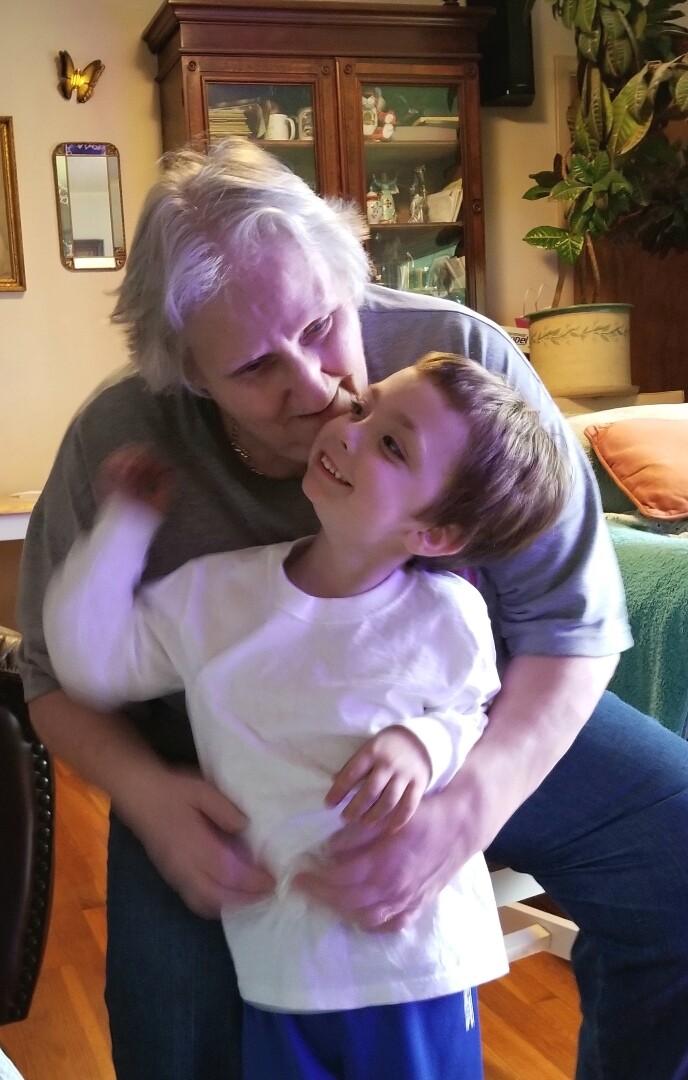 Older person with gray hair hugs a smiling child indoors, both facing each other in a cozy room.