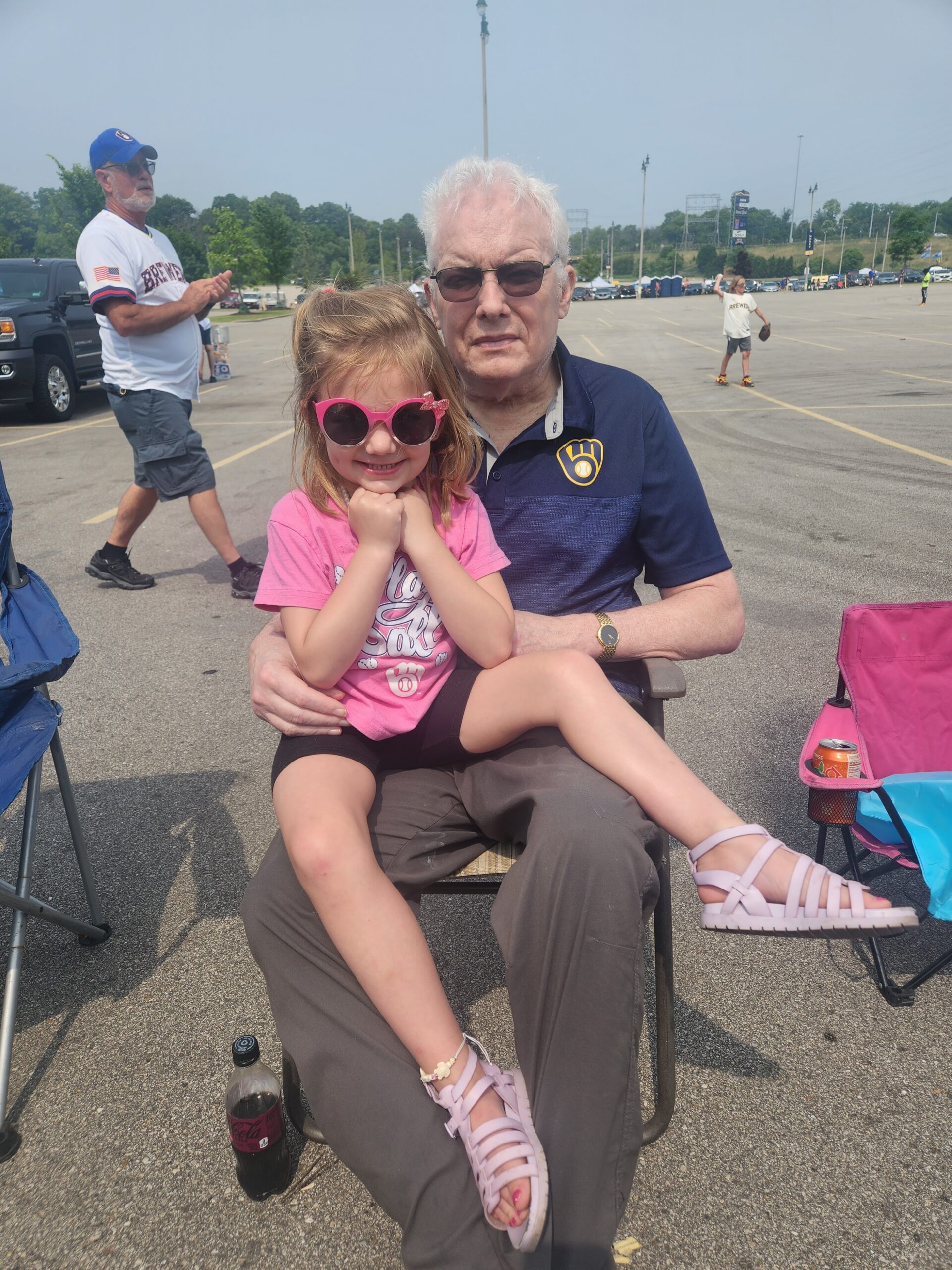 Grandfather and young girl sit together in a parking lot at an outdoor event, posing for the photo.