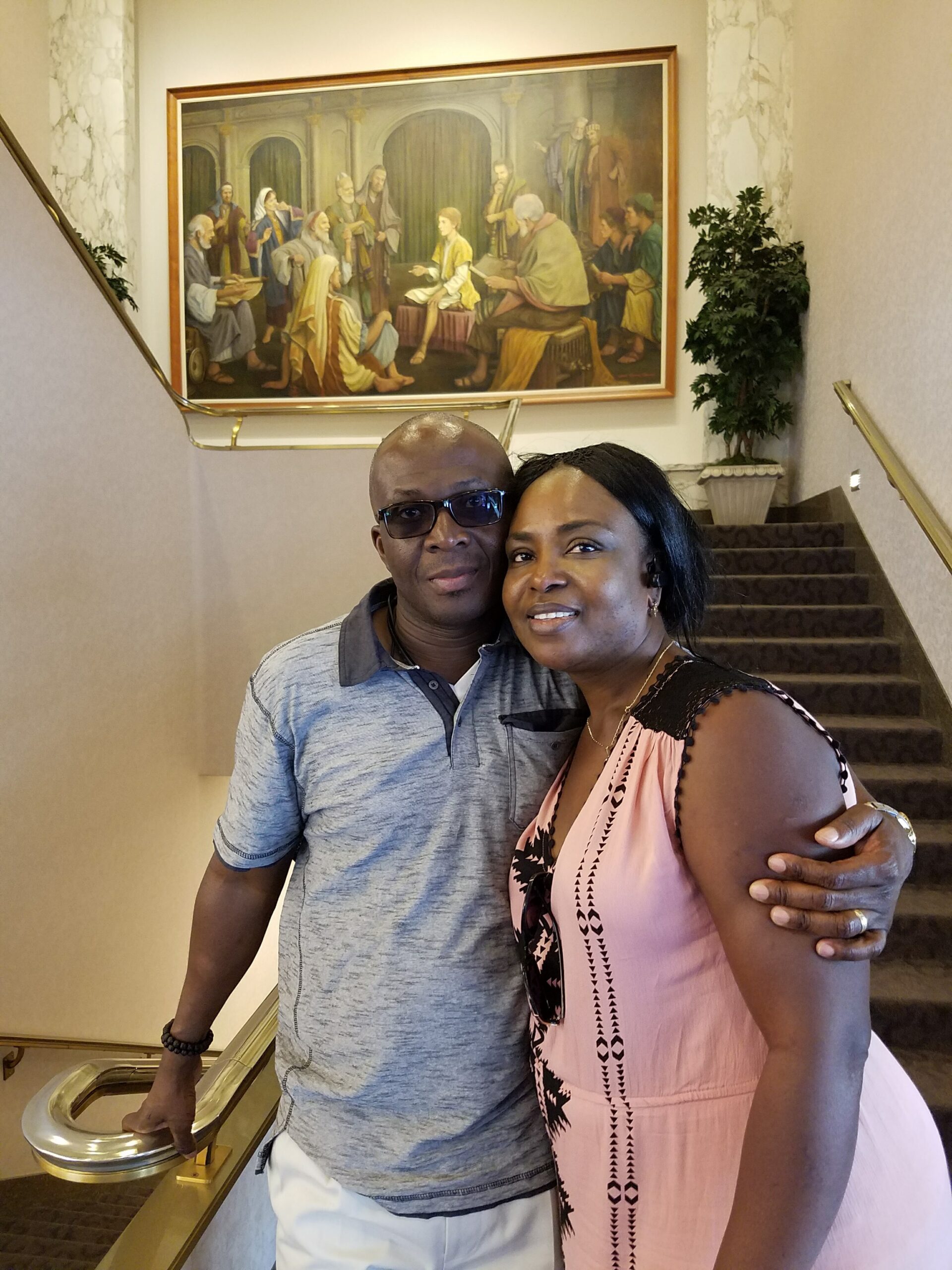 Couple posing on a hotel staircase in front of a large framed painting of The Last Supper on the wall behind them.