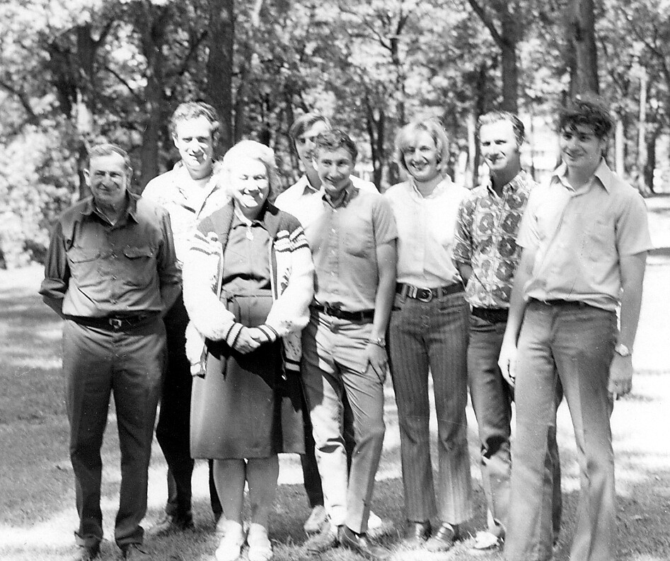 Group of eight people standing together outdoors in a park, smiling for the photo.