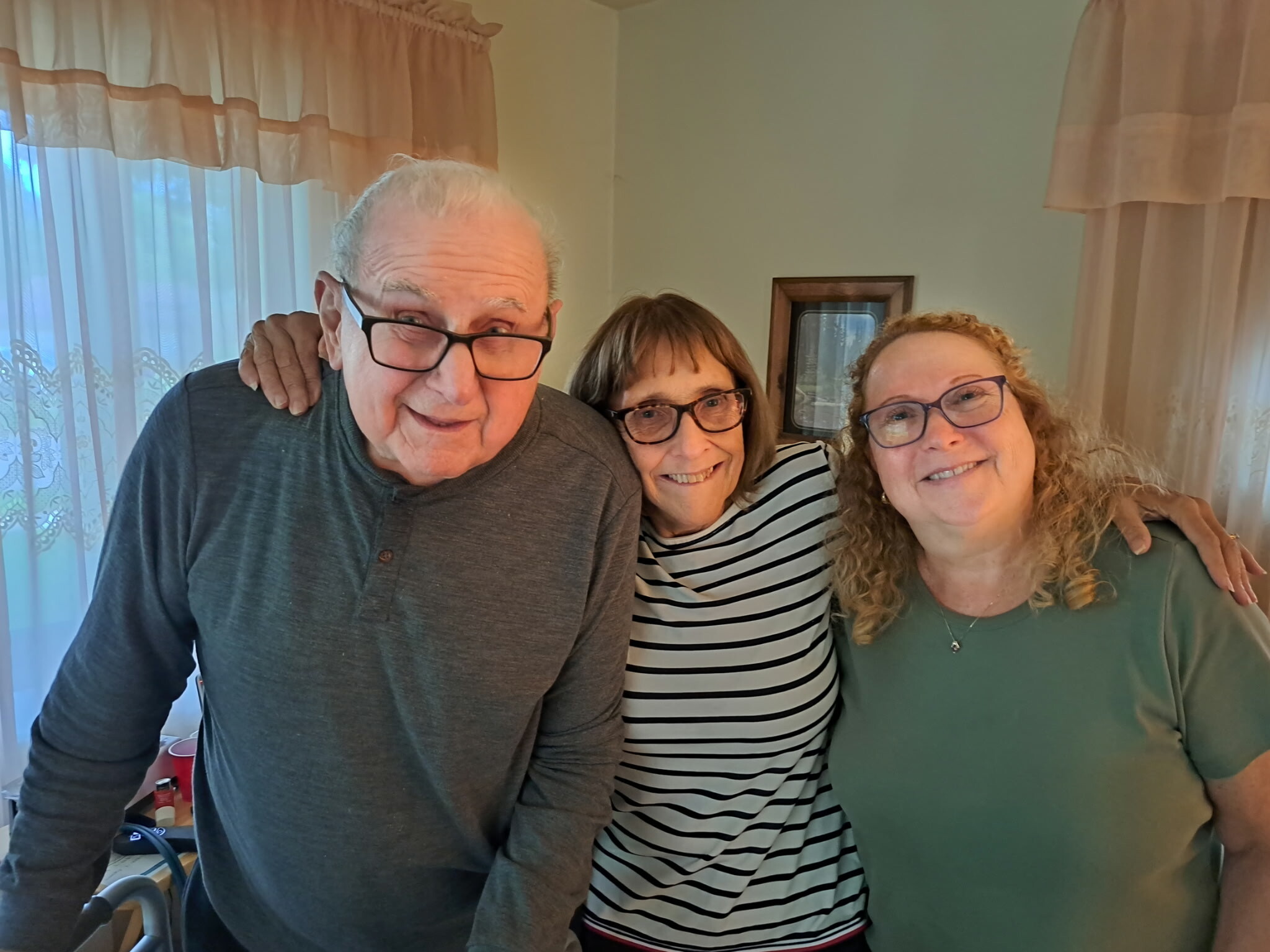 Three adults posing for a selfie indoors, smiling at the camera with light curtains in the background.