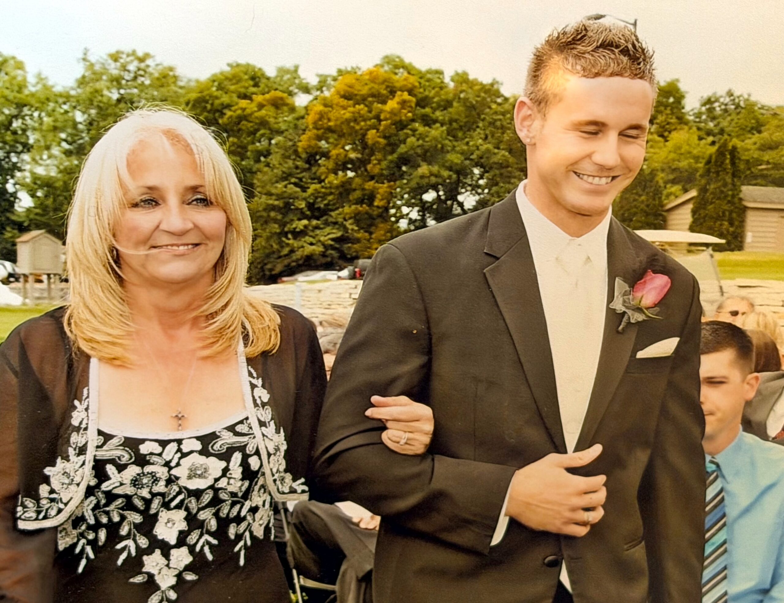 Smiling woman in a black floral dress linked arm-in-arm with a man in a suit at an outdoor event.