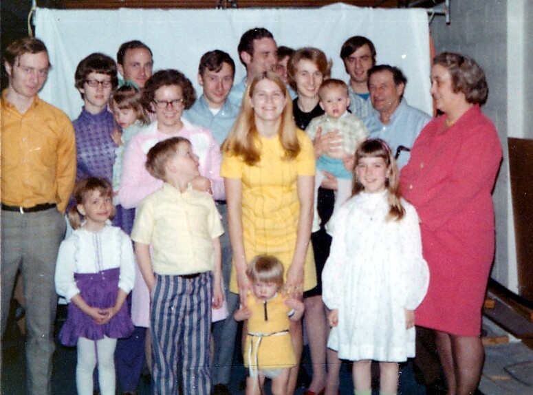 Large family group portrait with adults and children posing together in a living room setting.