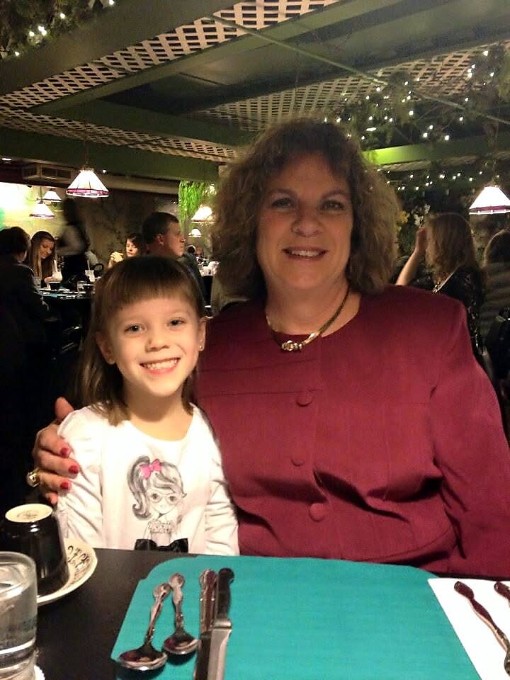 Smiling woman in burgundy jacket posing with a young girl at a restaurant table, arms around each other.