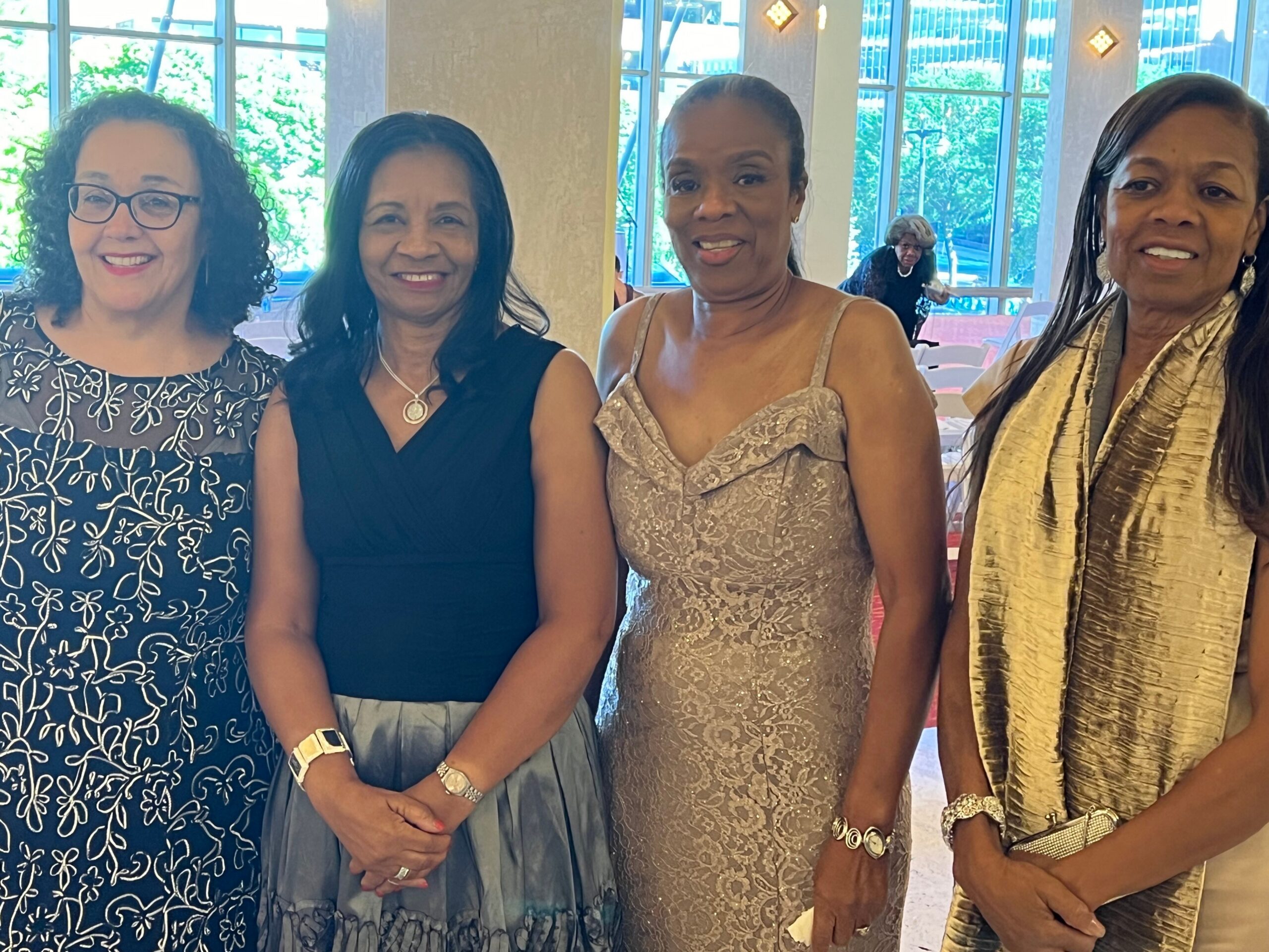 Four women in formal dresses posing together for a photo at an indoor event.
