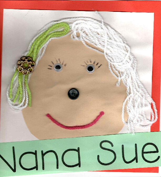 Smiling handmade face craft with white and green yarn hair, a flower hair clip, button nose, googly eyes, and a red yarn smile on a beige circle with a name banner.