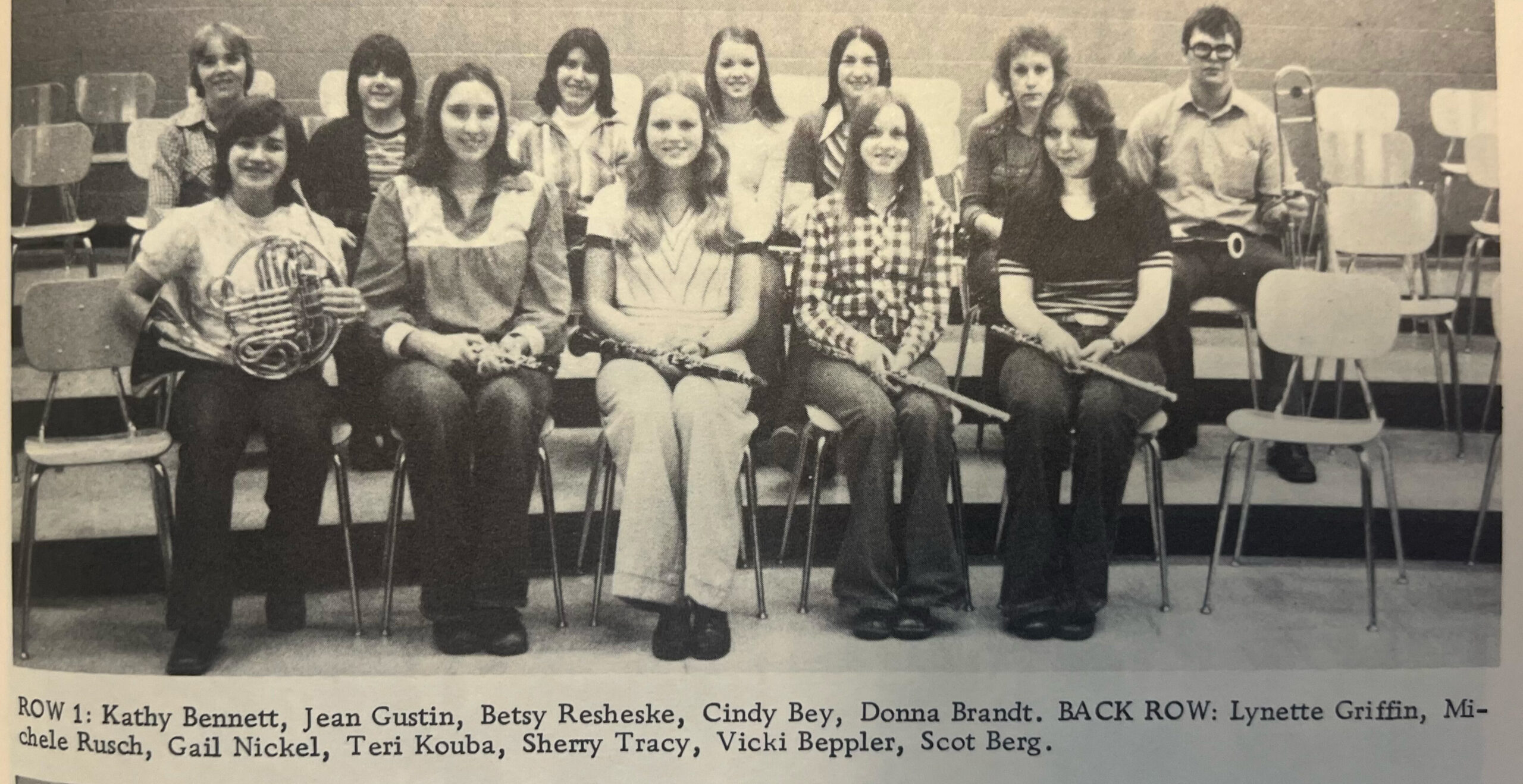 Group of students seated in a classroom posing for a band photo, front row holding woodwind instruments (clarinets).