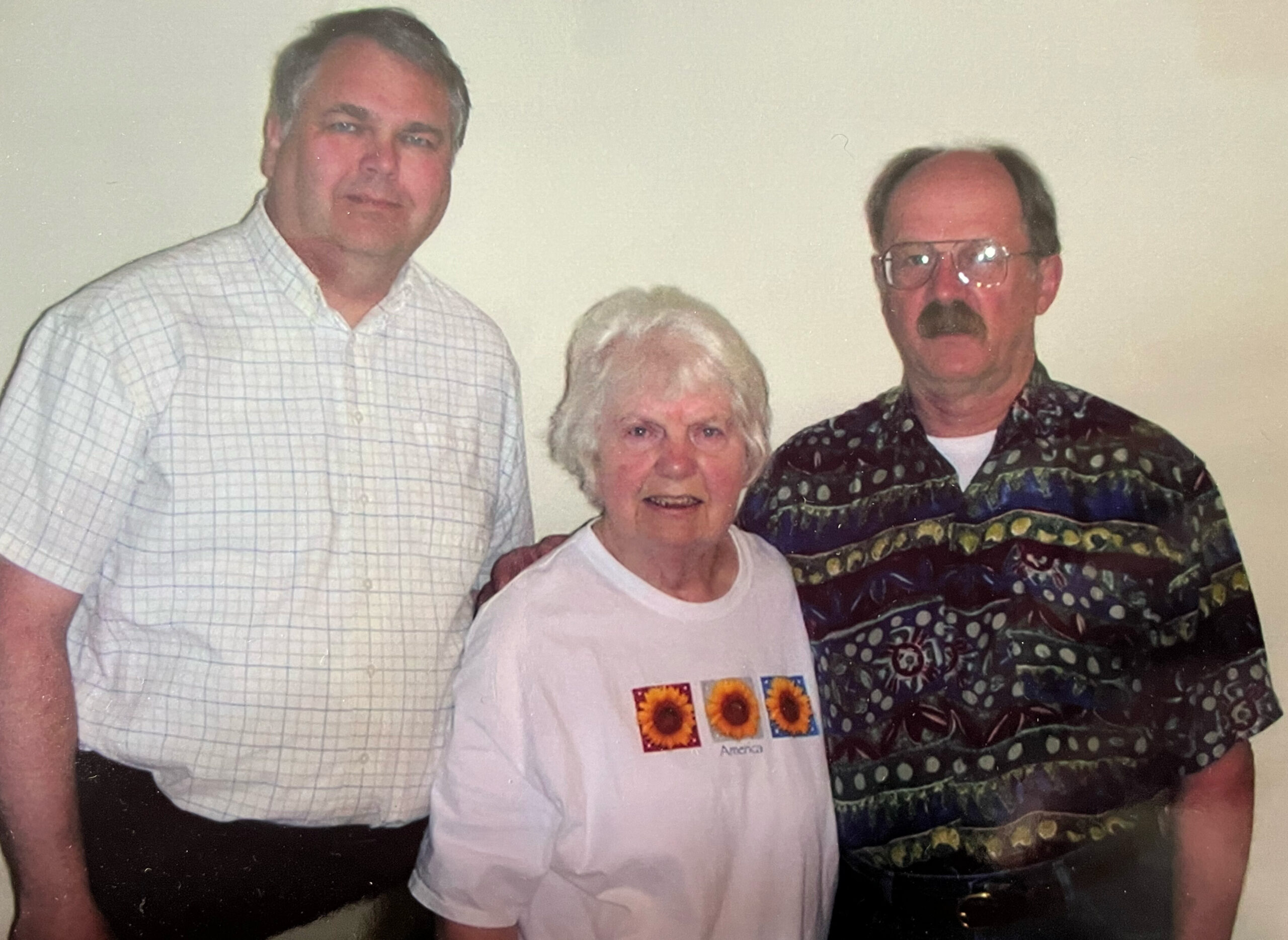 Three adults posing together in a casual photo: woman in white center, men on either side.