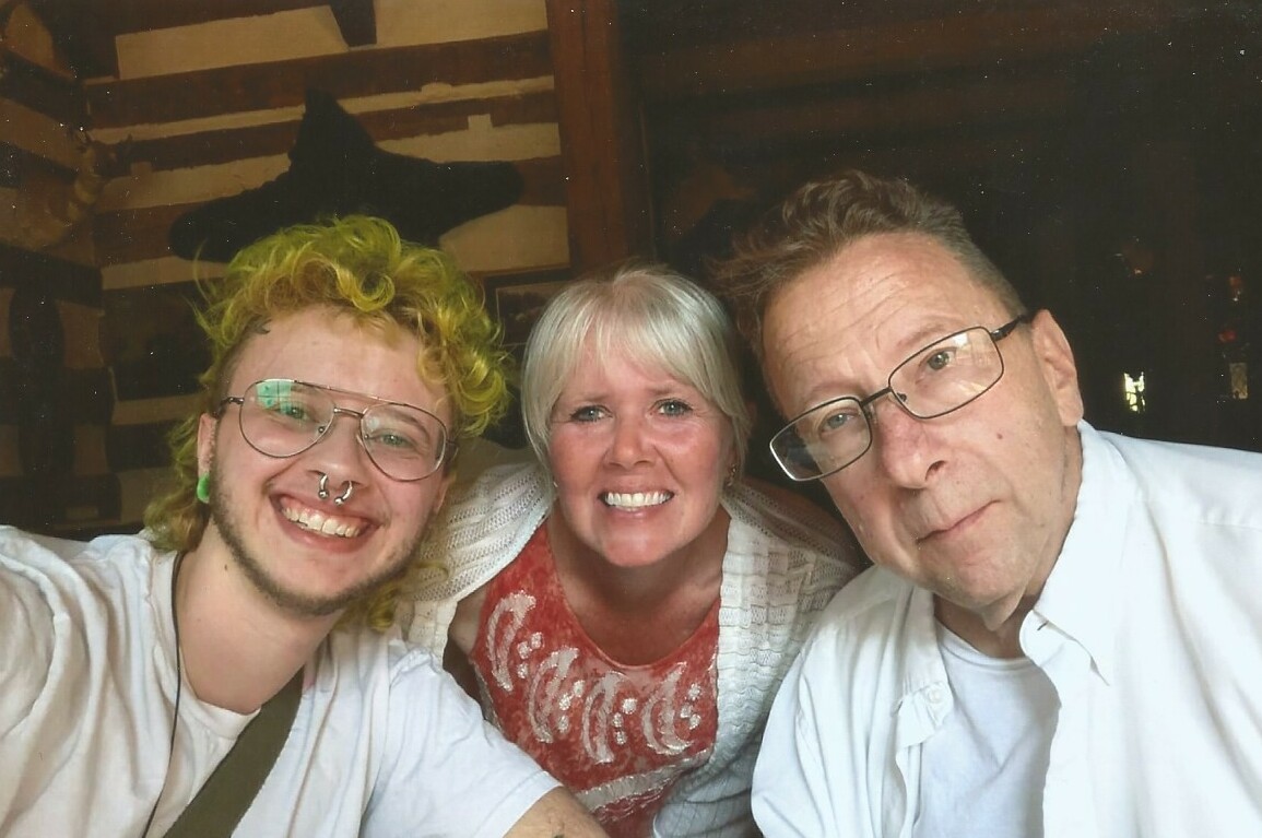 Three people smiling at the camera in a rustic wooden interior, taking a selfie.