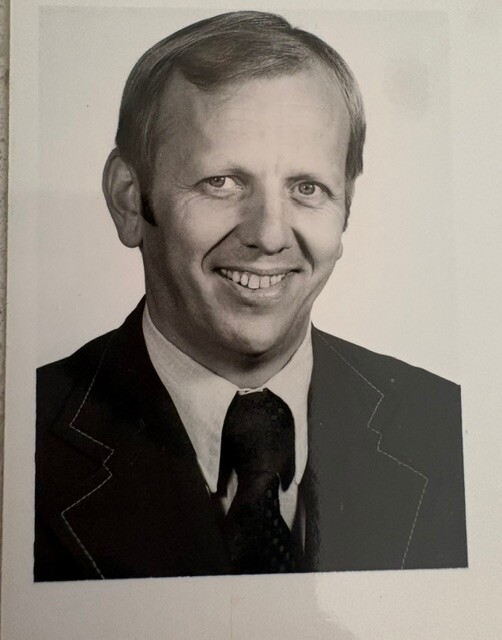 Black-and-white portrait of a smiling man in a suit and tie, facing the camera.