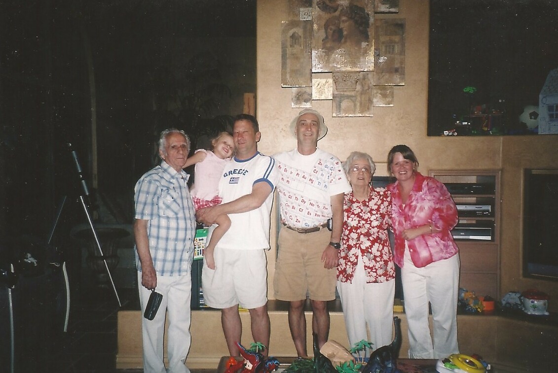 Six people posing together in a living room, a little girl held by a man, all smiling at the camera.