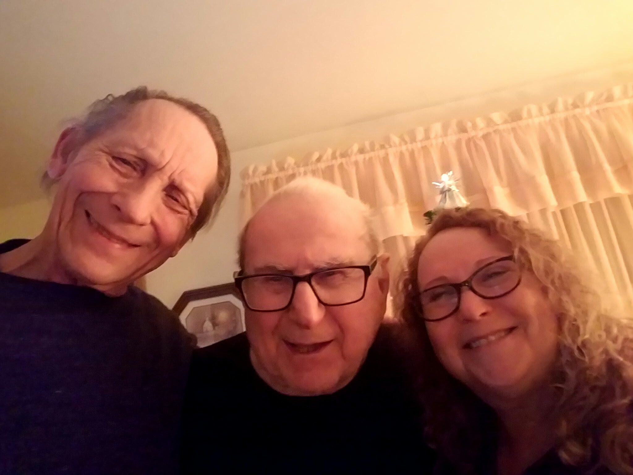 Group selfie of four adults smiling at the camera indoors, beige curtains in the background.