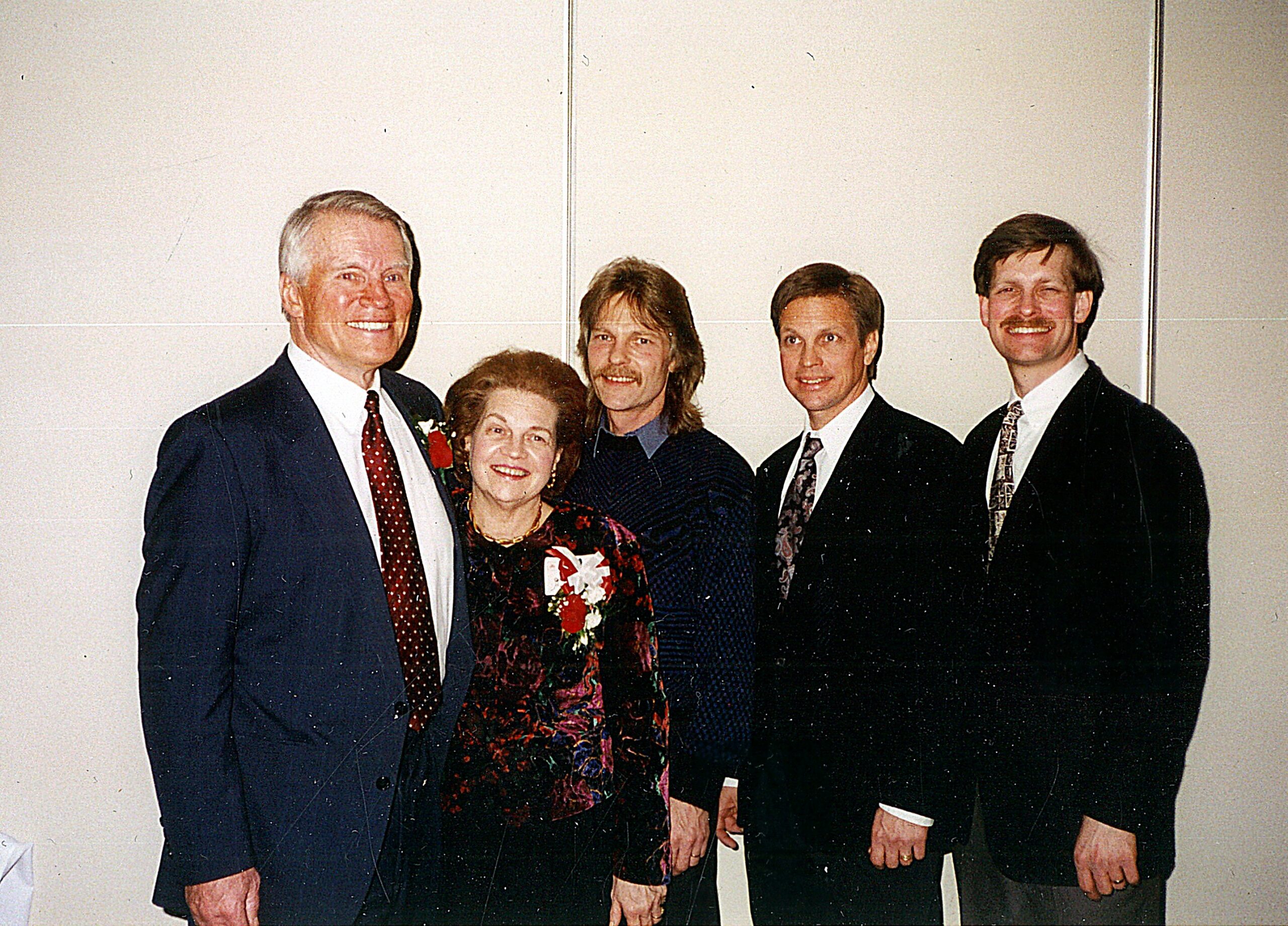 Group of five adults in formal attire posing for a group portrait indoors at an event.