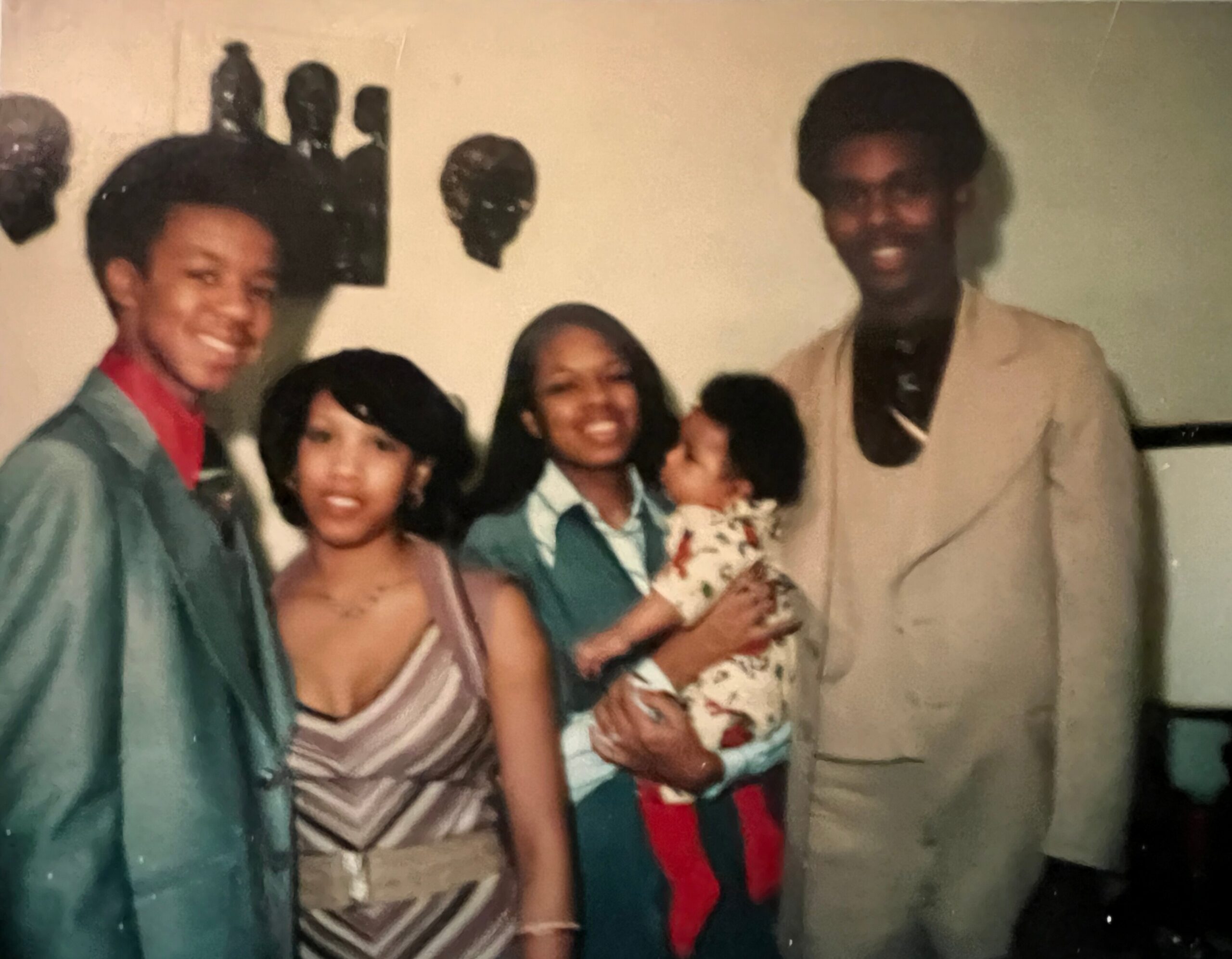 Group of smiling friends posing closely for a photo at a party, wearing colorful outfits including teal jackets and striped dresses.