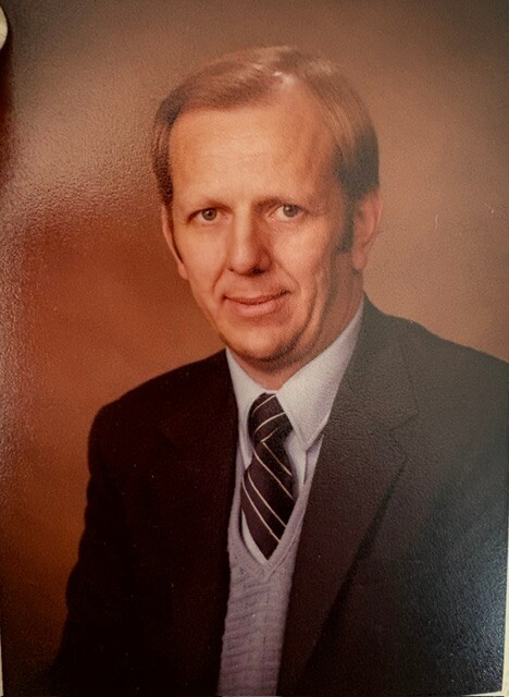 Portrait of a middle-aged man in a dark suit, light sweater, and striped tie, posing for a formal photo.