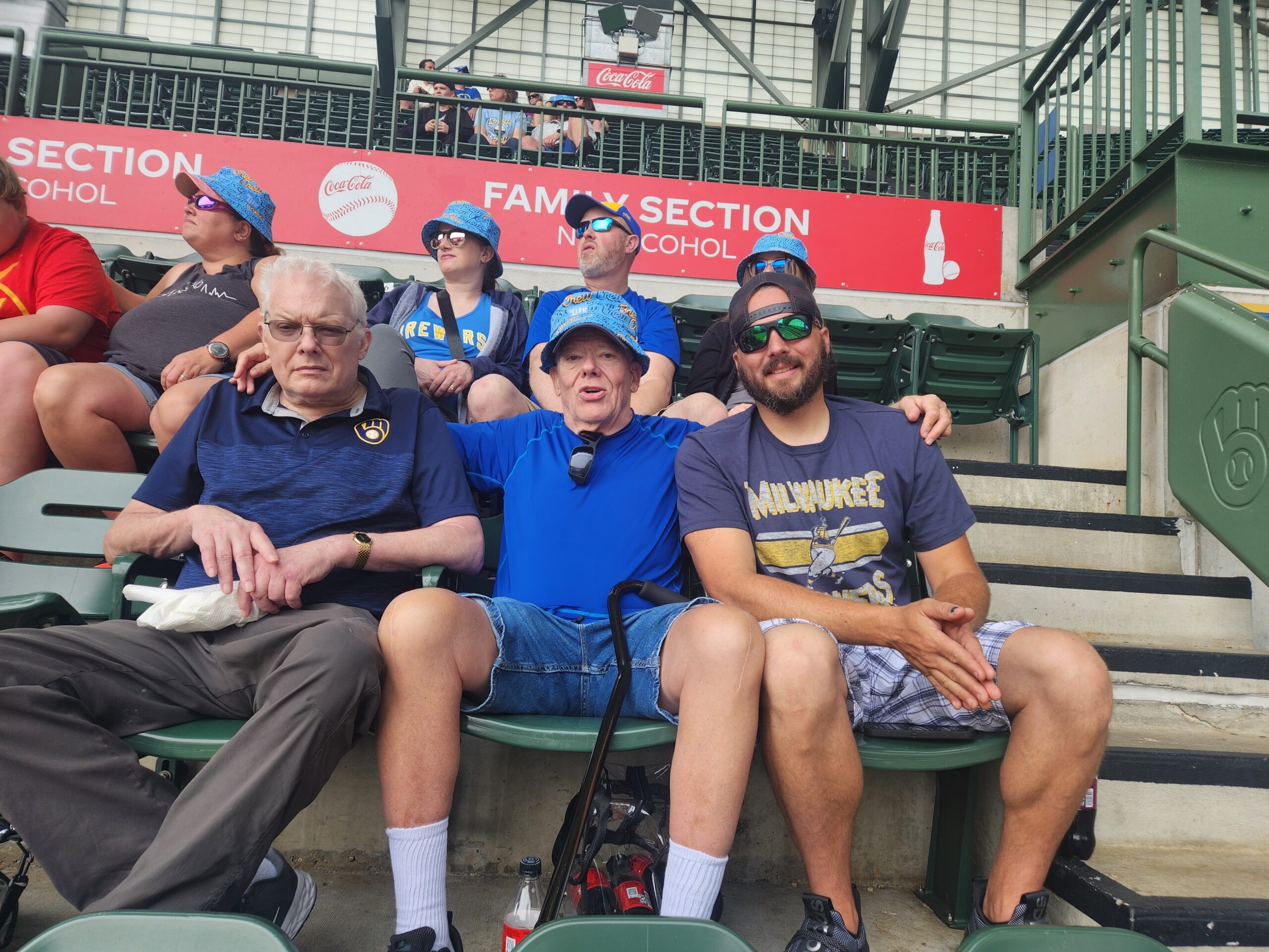 Group of spectators in stadium seats, wearing blue hats, near a red Family Section sign and Coke ad.