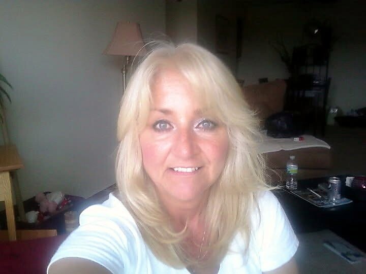 Self-portrait of a smiling blonde woman in a bright living room, taking a selfie.