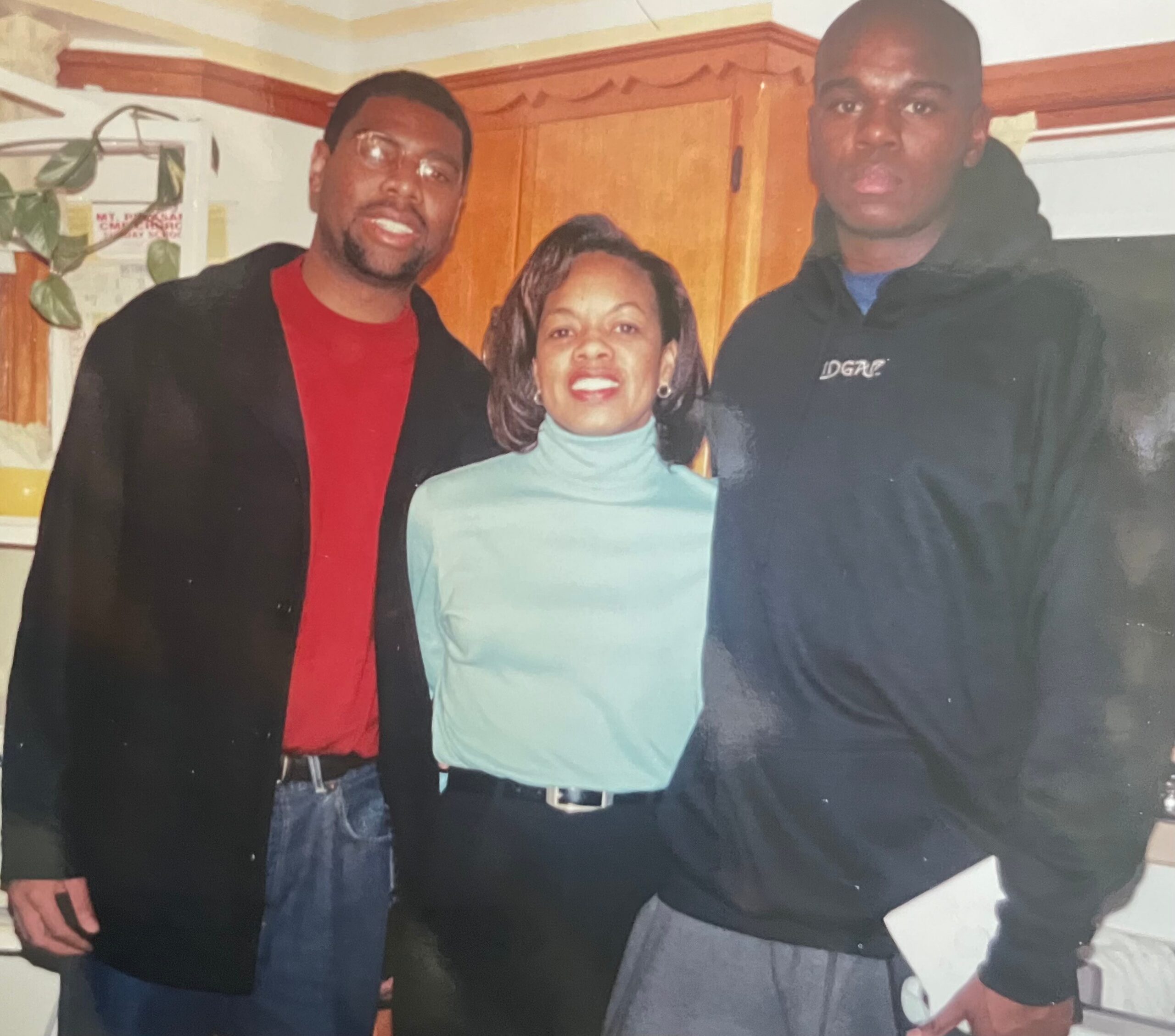 Three adults posing together in a home kitchen, smiling at the camera. index:1