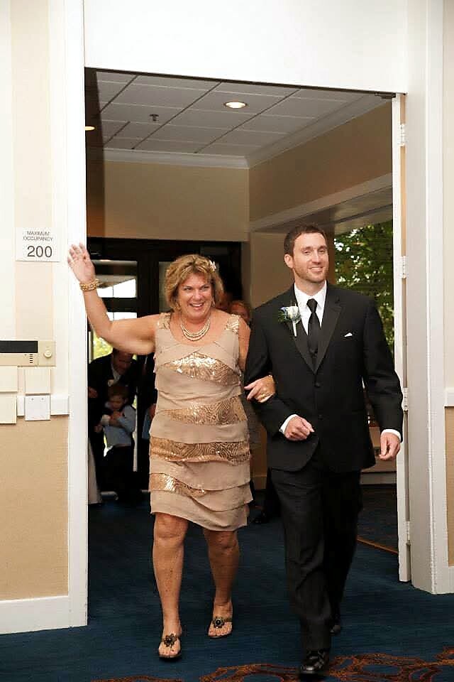Smiling woman in a beige sequined dress walks arm-in-arm with a man in a black suit as they enter a doorway at a formal event.