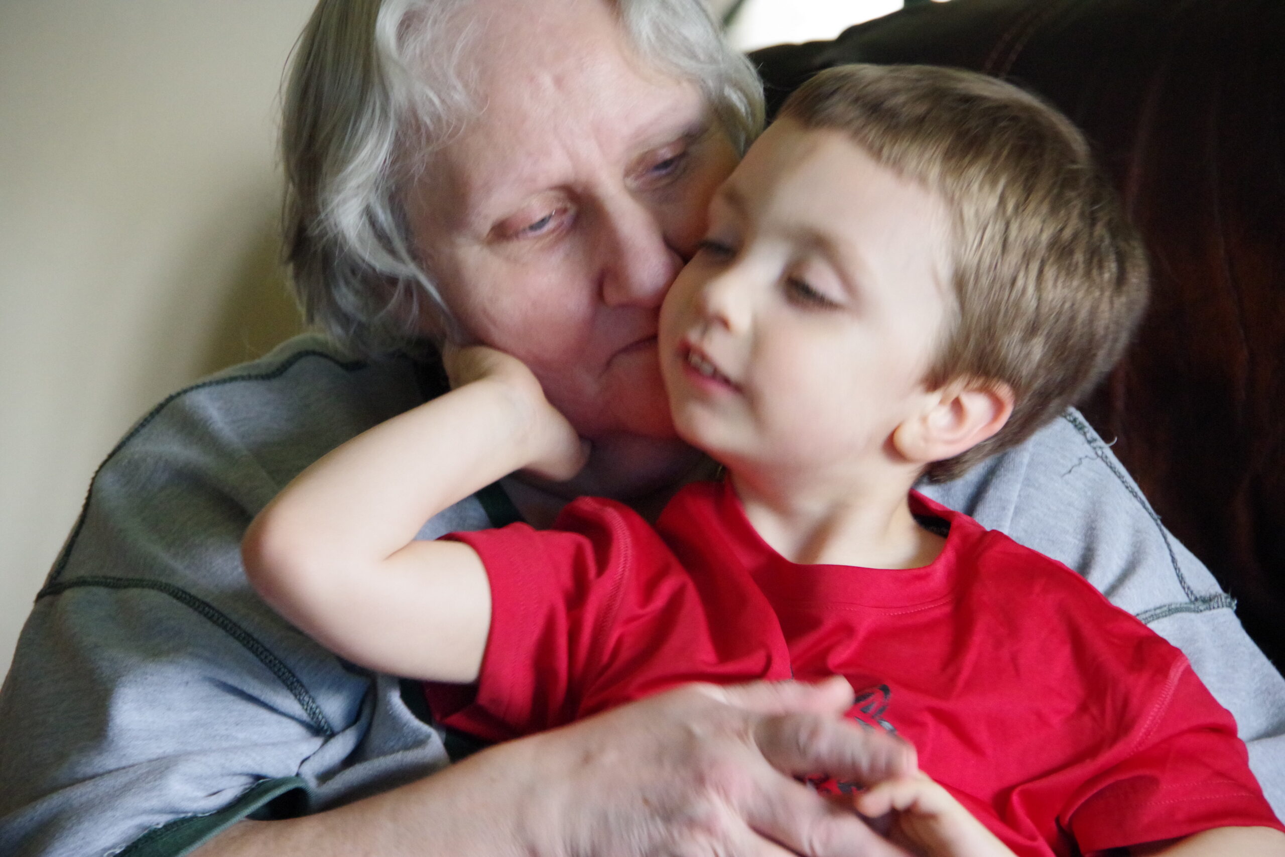 Grandparent cuddling and kissing a young boy on the cheek while sitting together, warm and affectionate moment.