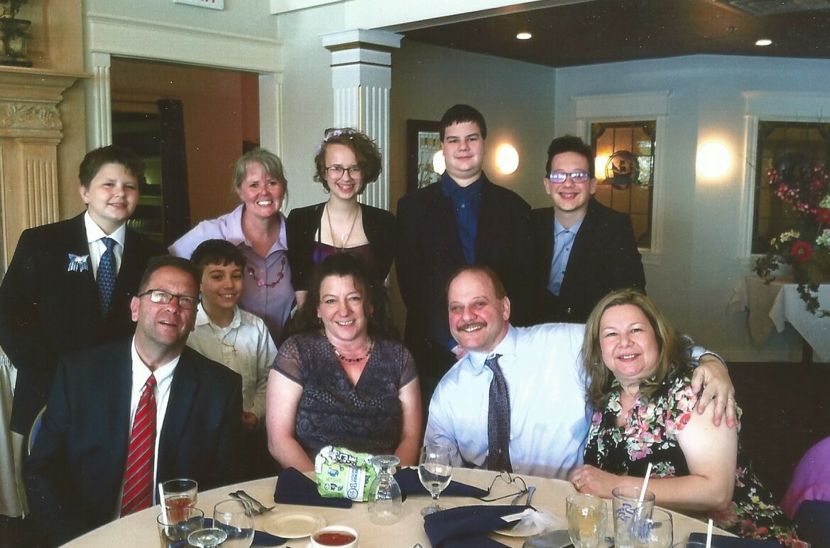 Group of ten people posing for a photo at a formal dinner, some seated and others standing, all smiling at the camera.