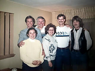 Six people posing for a group photo in a living room, smiling at the camera.