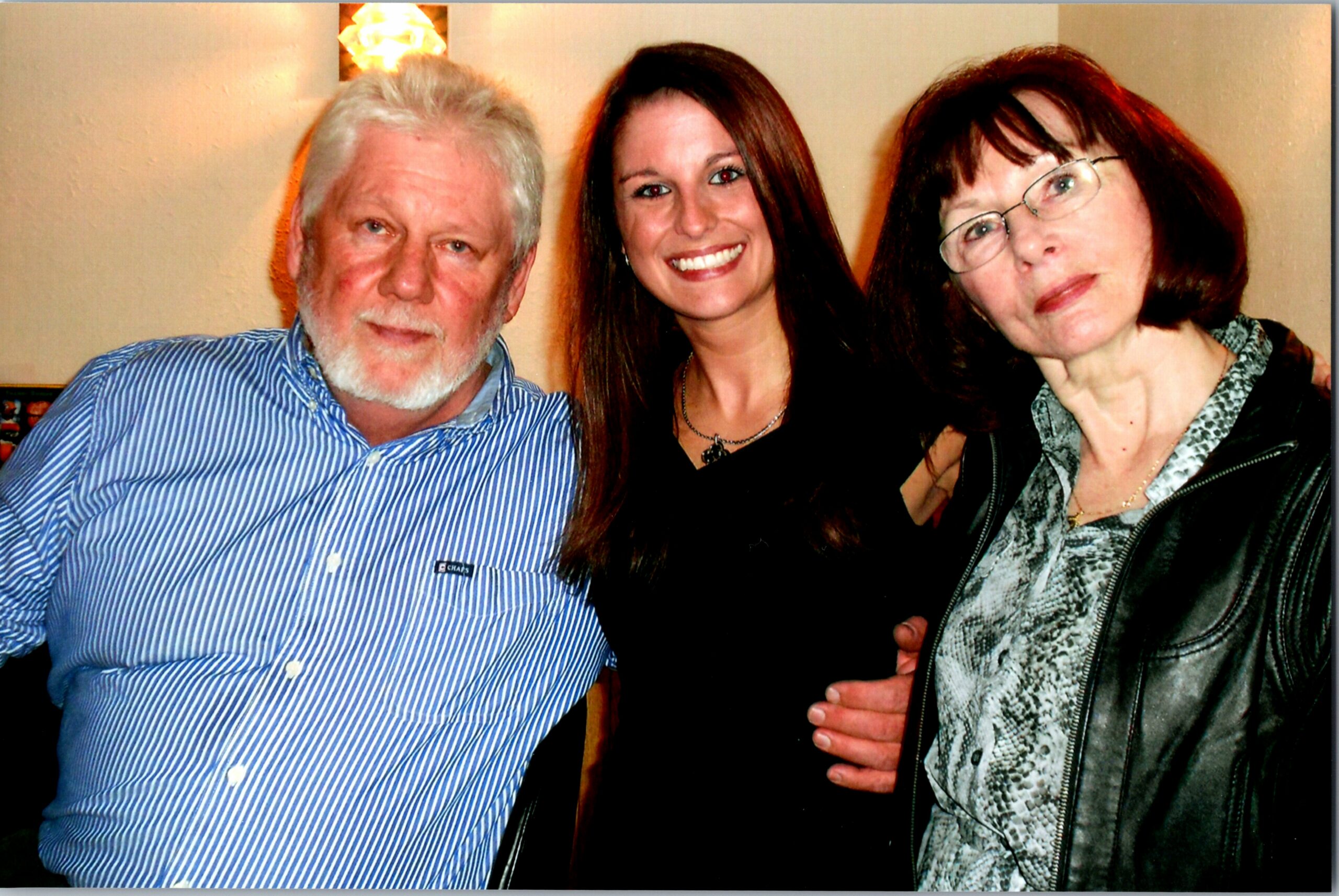 Three adults posing together for a photo: an older man in a blue striped shirt, a smiling young woman, and a woman with glasses on the right.