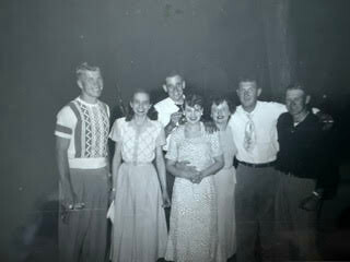 Black-and-white photo of eight adults in vintage clothing posing together at a social event.