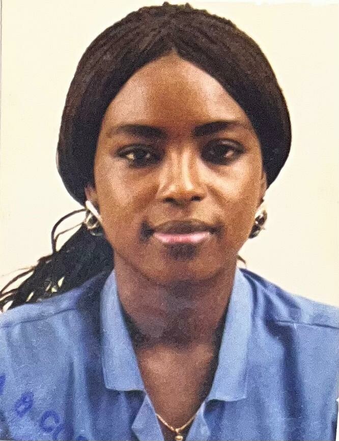 Portrait of a woman with braided hair and hoop earrings, wearing a blue uniform shirt, facing the camera.