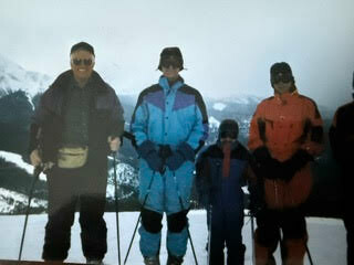 Four skiers in colorful jackets and goggles stand on a snowy mountainside, posing for a photo.