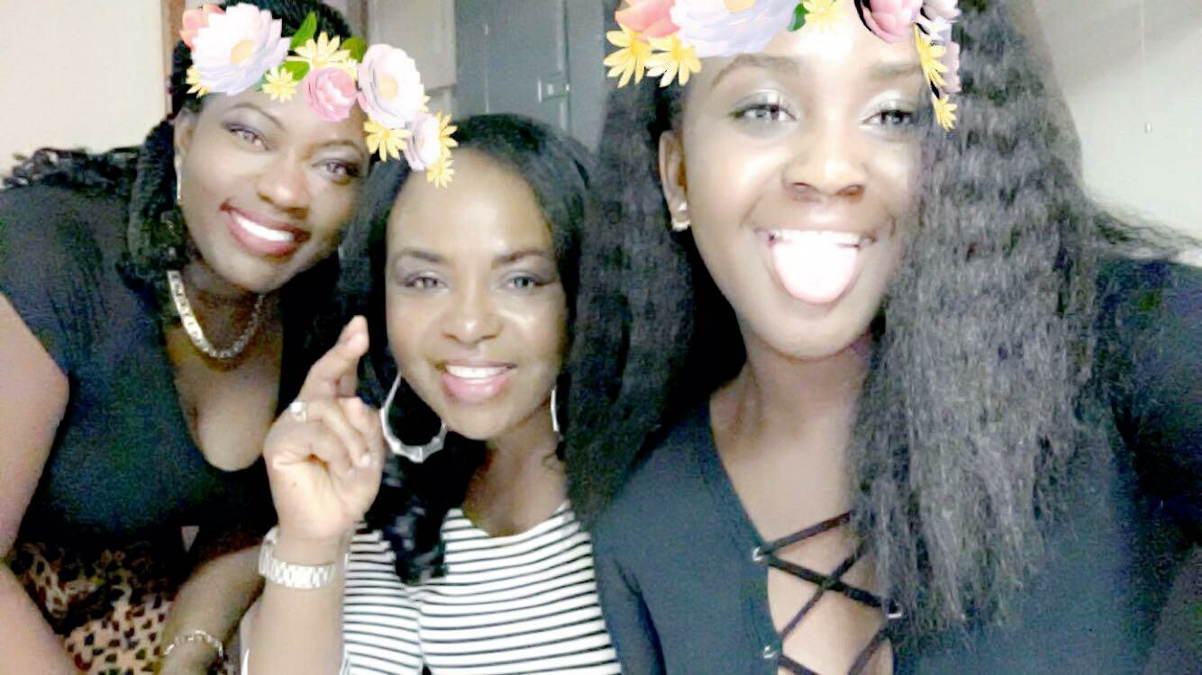 Three women posing for a selfie, wearing flower crown filters and smiling warmly in a bright setting.