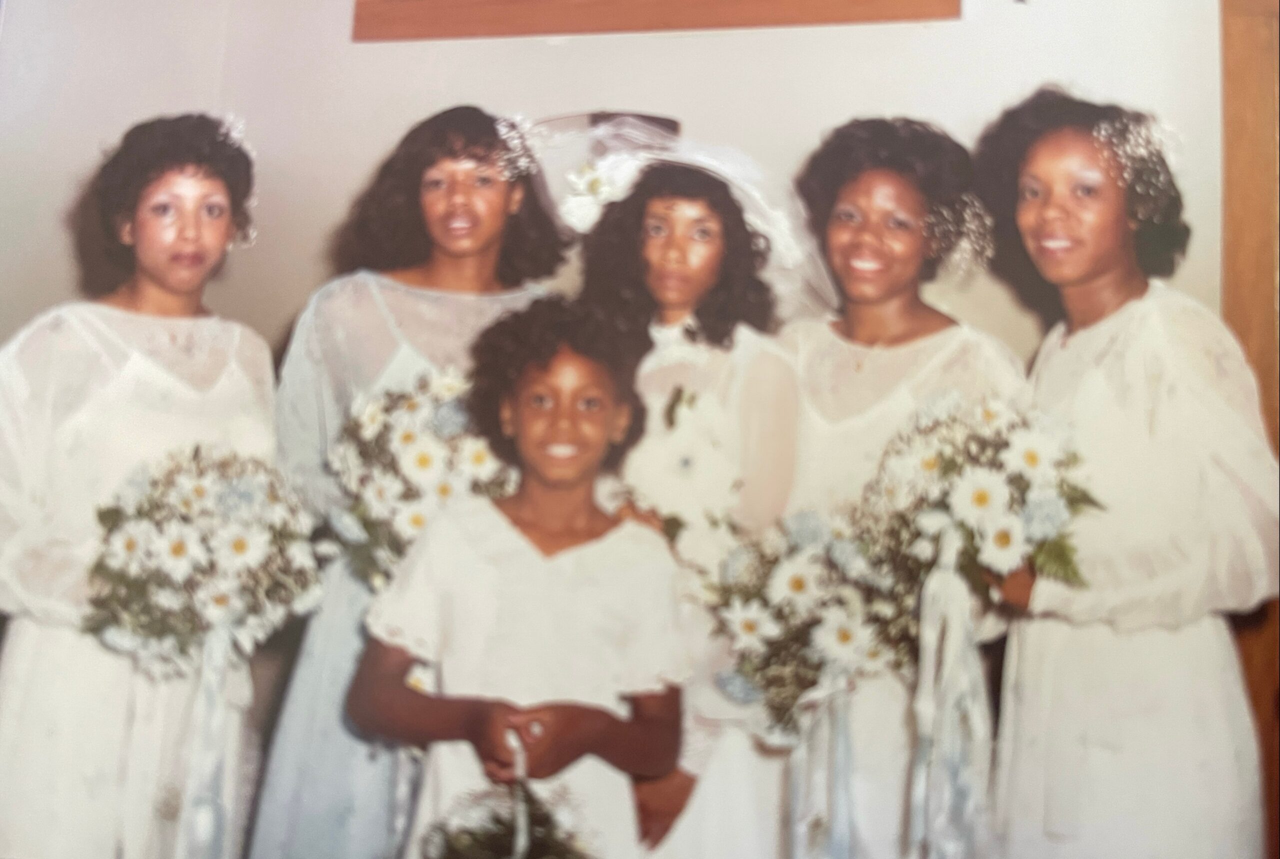 Group of bridesmaids in white dresses posing with bouquets at a wedding.
