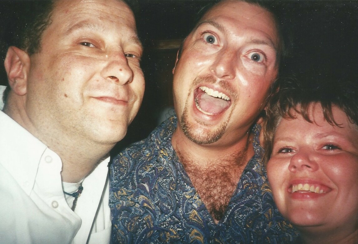 Three friends close together, smiling widely for a selfie at a casual gathering.
