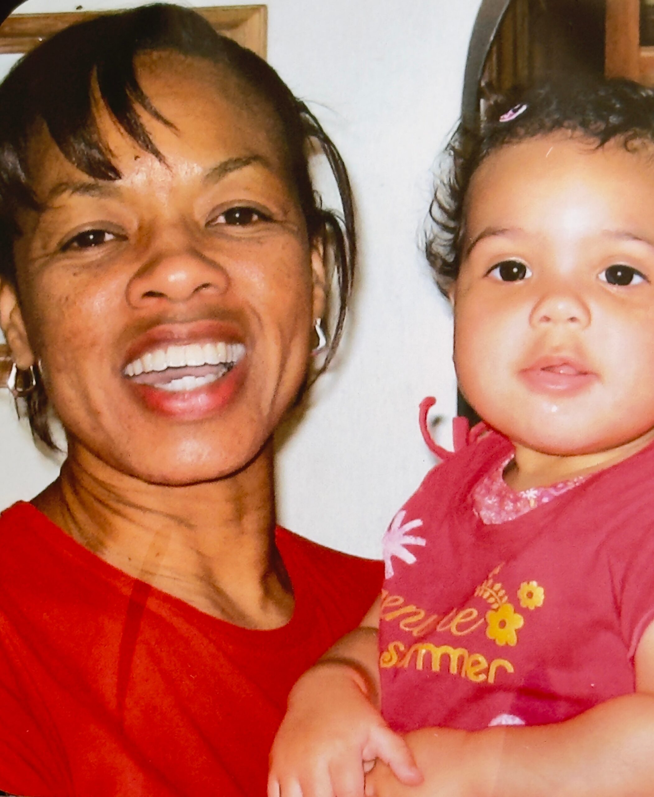 Close-up of a smiling adult woman and young child in red and pink clothing flashing smiles at the camera.
