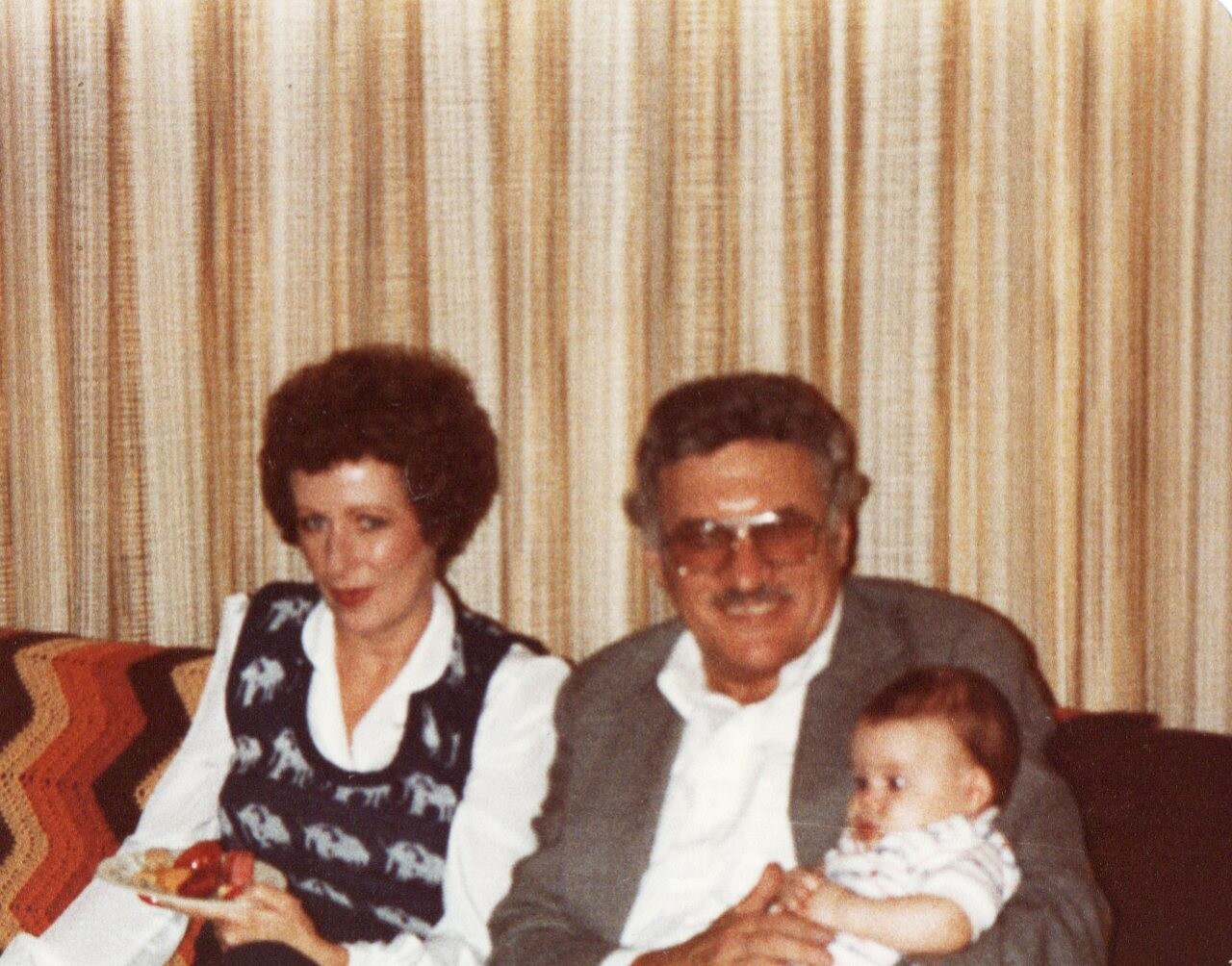 Woman and man sit on a striped couch with a baby, posing for a family photo in a living room.