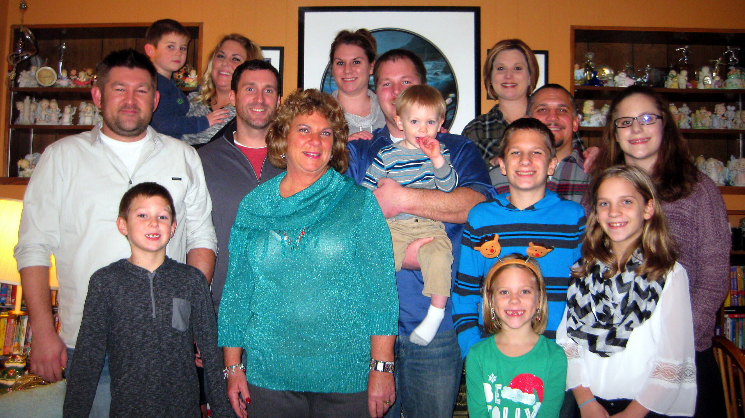 Large family group posing for a photo in a warmly lit living room with shelves of figurines in the background.