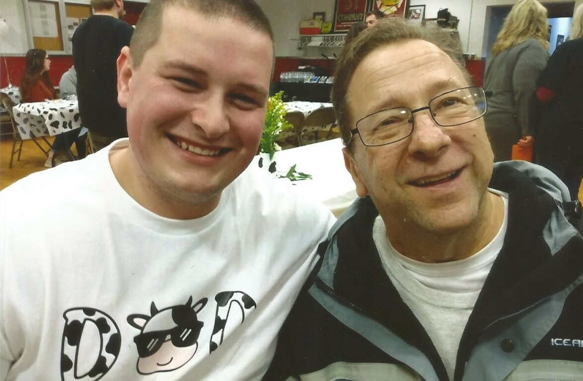 Two men smiling for a photo at a social event, seated at a table with decorations in the background.