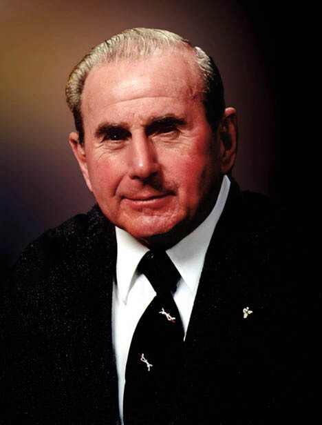 Formal portrait of an older man wearing a black suit and white shirt, looking at the camera with a slight smile.