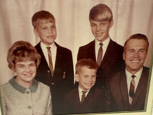 Family portrait in a studio: mother on left, three sons in the middle, father on the right, all in formal clothing.