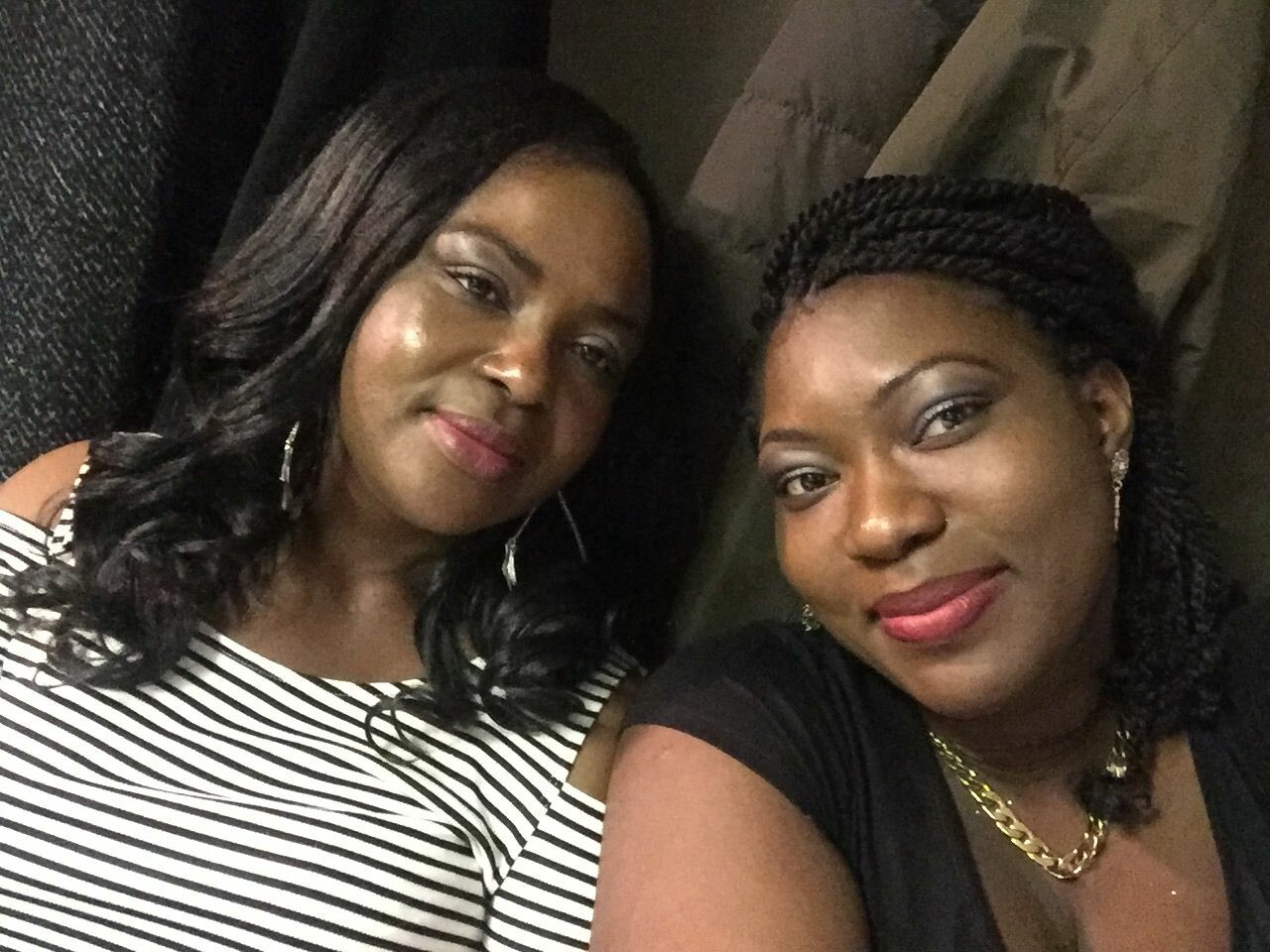 Two women posing for a selfie, smiling at the camera, one in a striped off-shoulder top and the other in a black top with gold jewelry.
