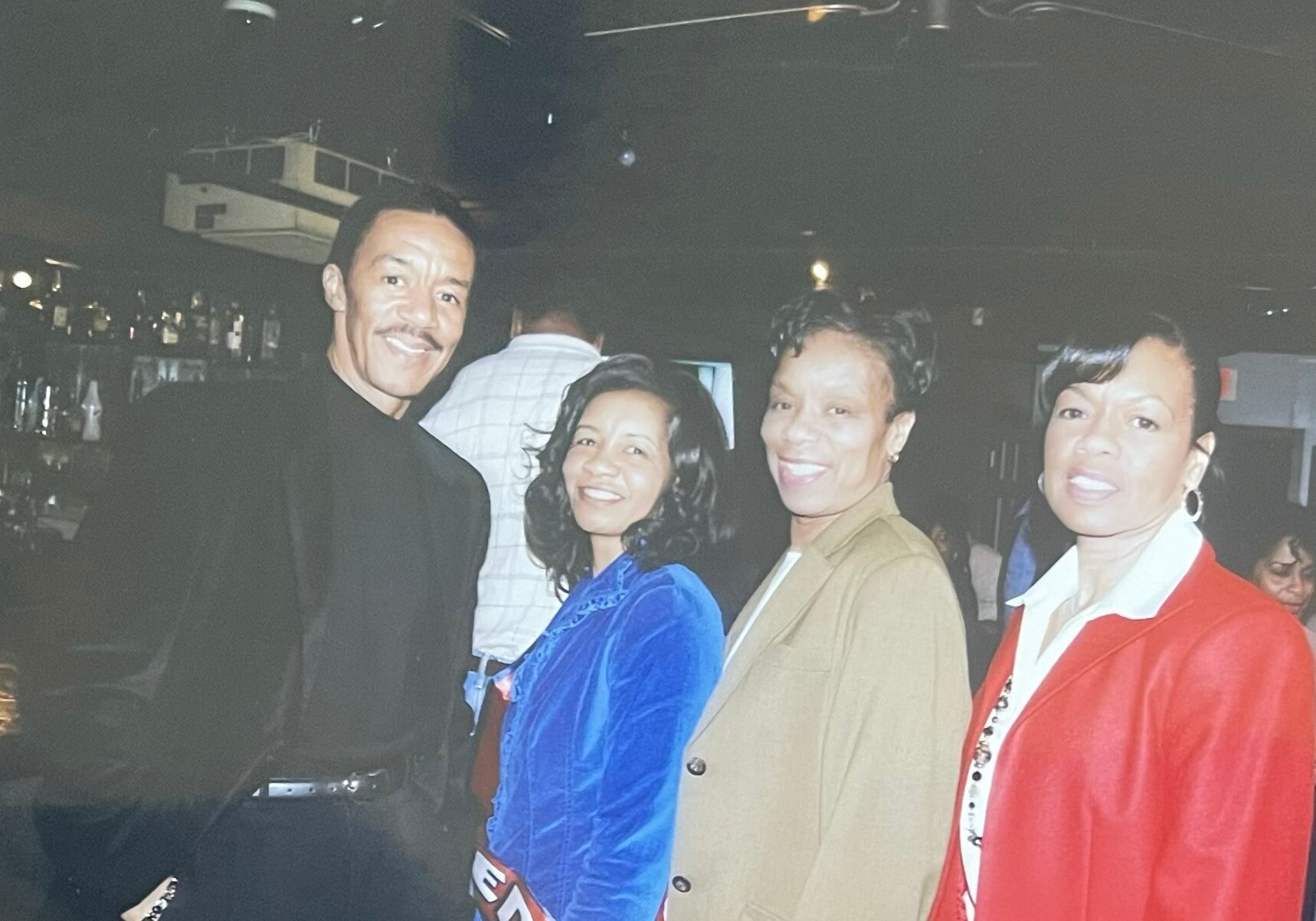 Four adults posing together at a dimly lit bar, smiling for the photo.