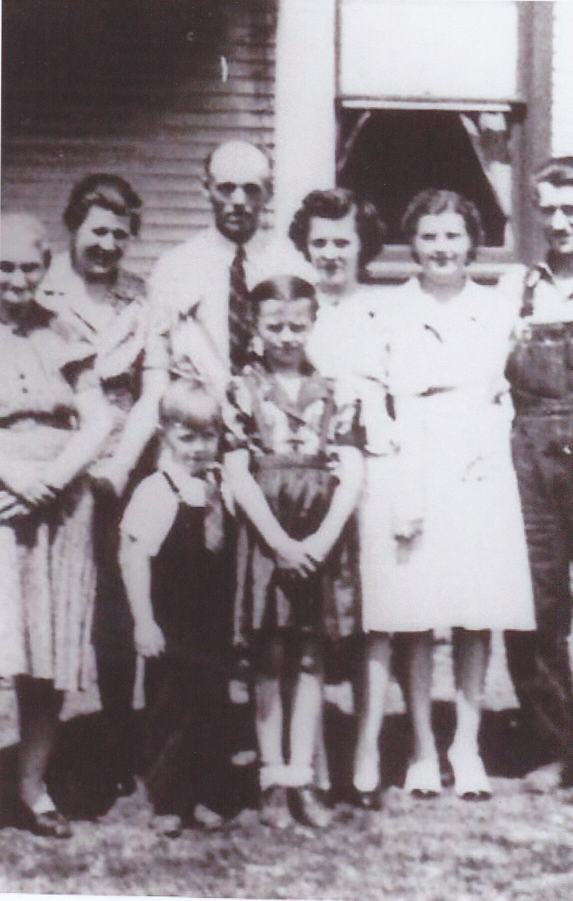 Black-and-white group photo of a family standing outside a house, with adults and children posing together.