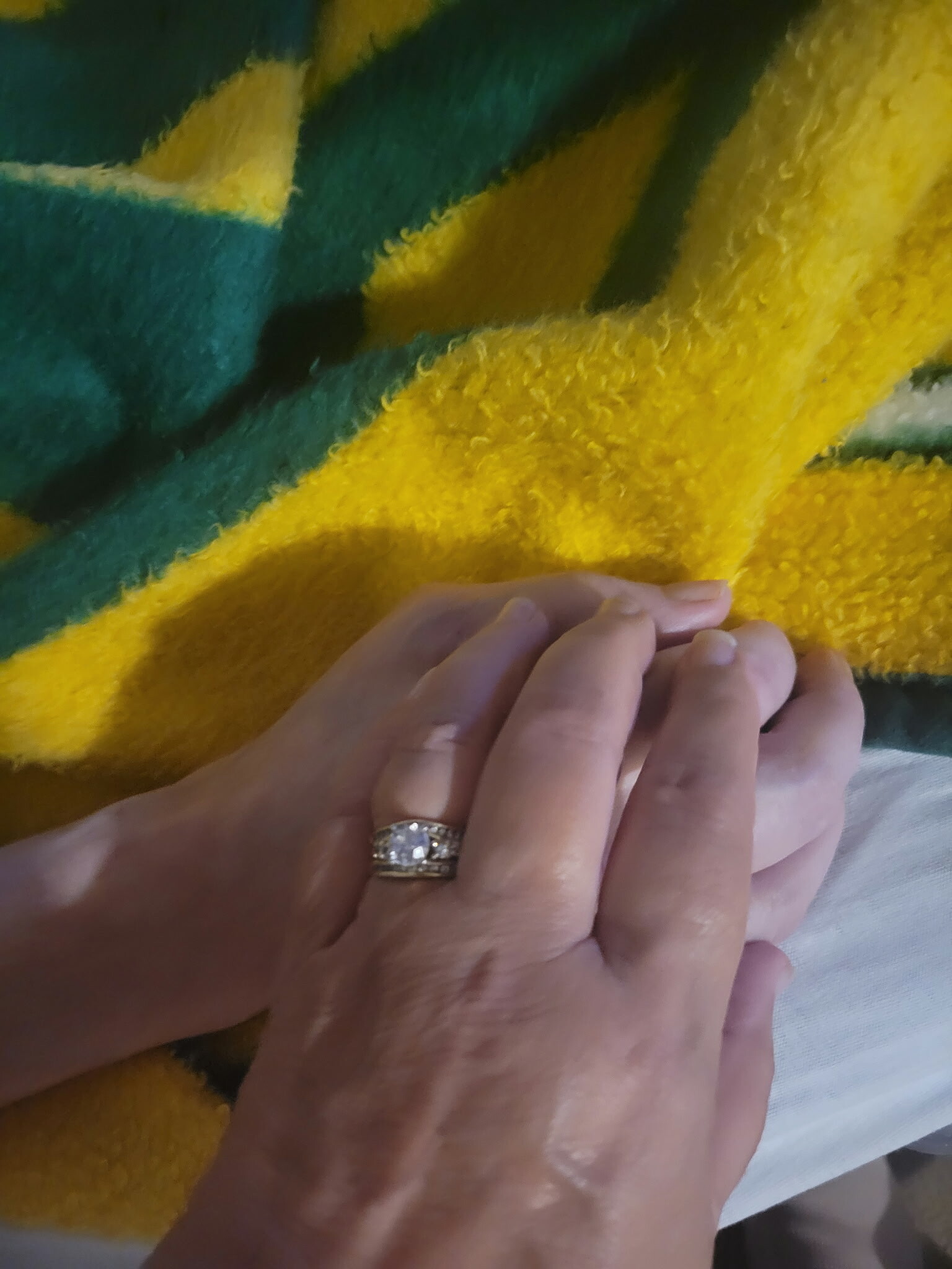 Close-up of a person's hands resting on a fuzzy yellow-and-green striped blanket, showcasing a diamond ring on the ring finger.