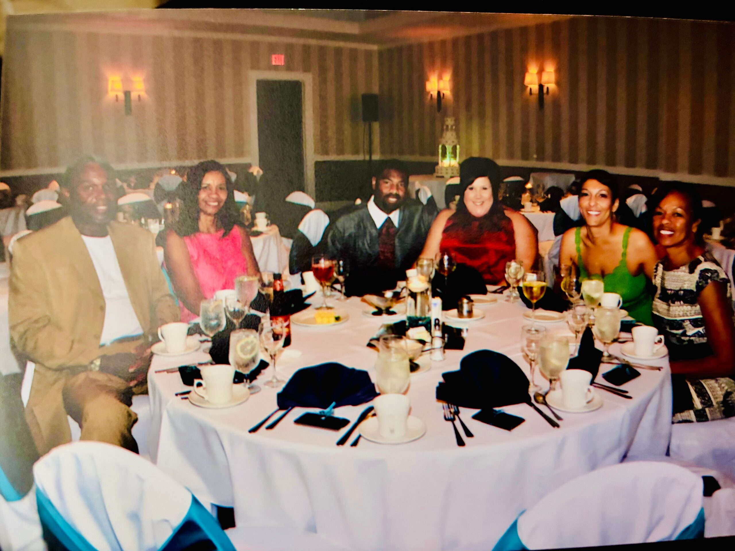 Group of smiling adults seated around a round banquet table at a formal event indoors, with dishes and drinks visible on the table.