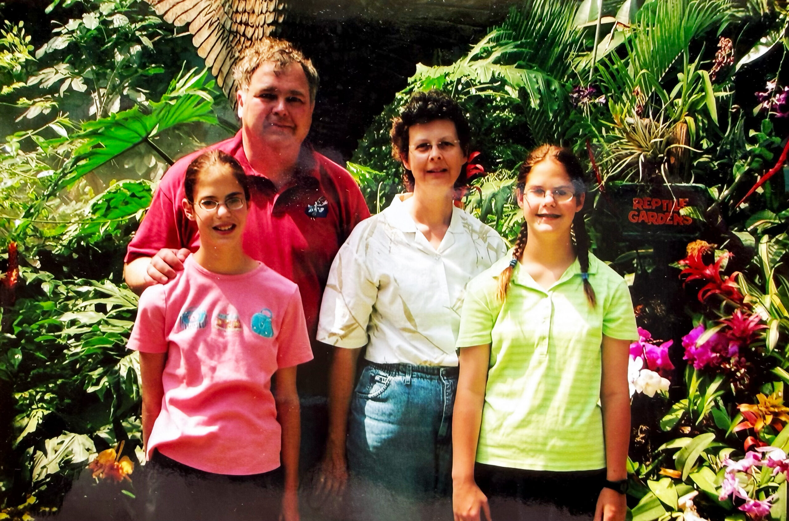 Four people posing together in a lush tropical garden with dense greenery and colorful flowers behind them.