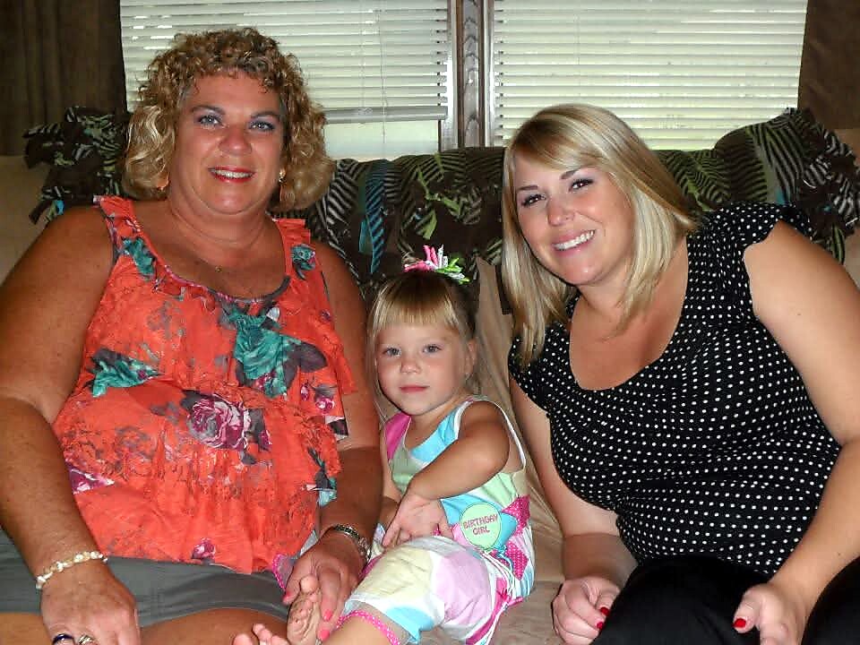 Three generations of women sit on a couch, smiling at the camera in a living room portrait.