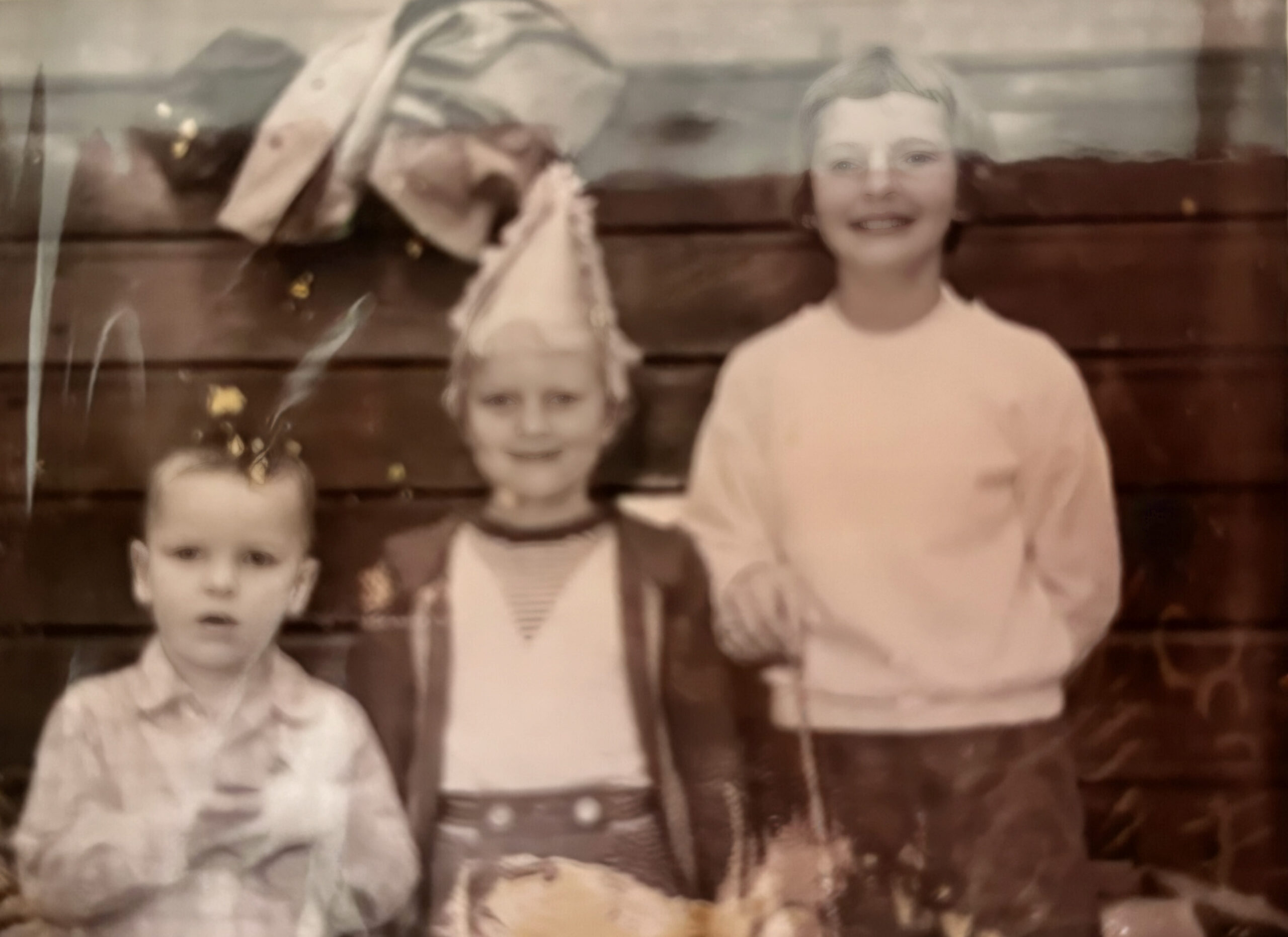 Faded, sepia-toned vintage photo of several children posing in front of a wooden wall backdrop.